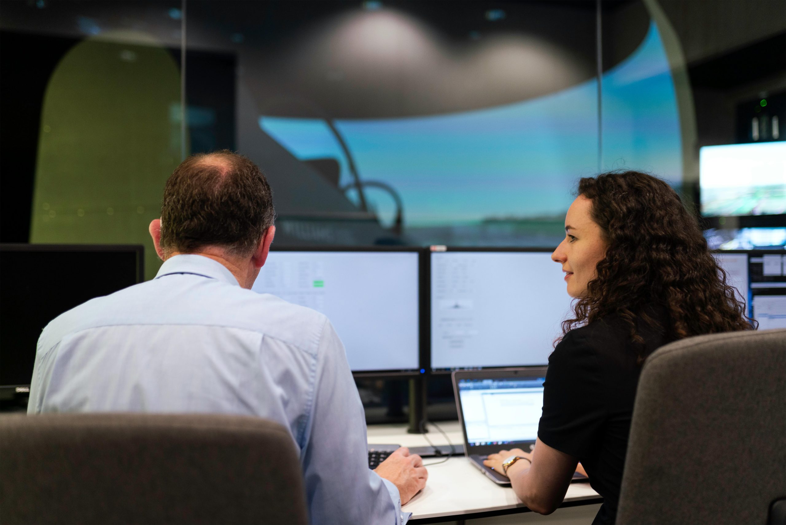 Two engineers working together on a computer simulation in a control room.