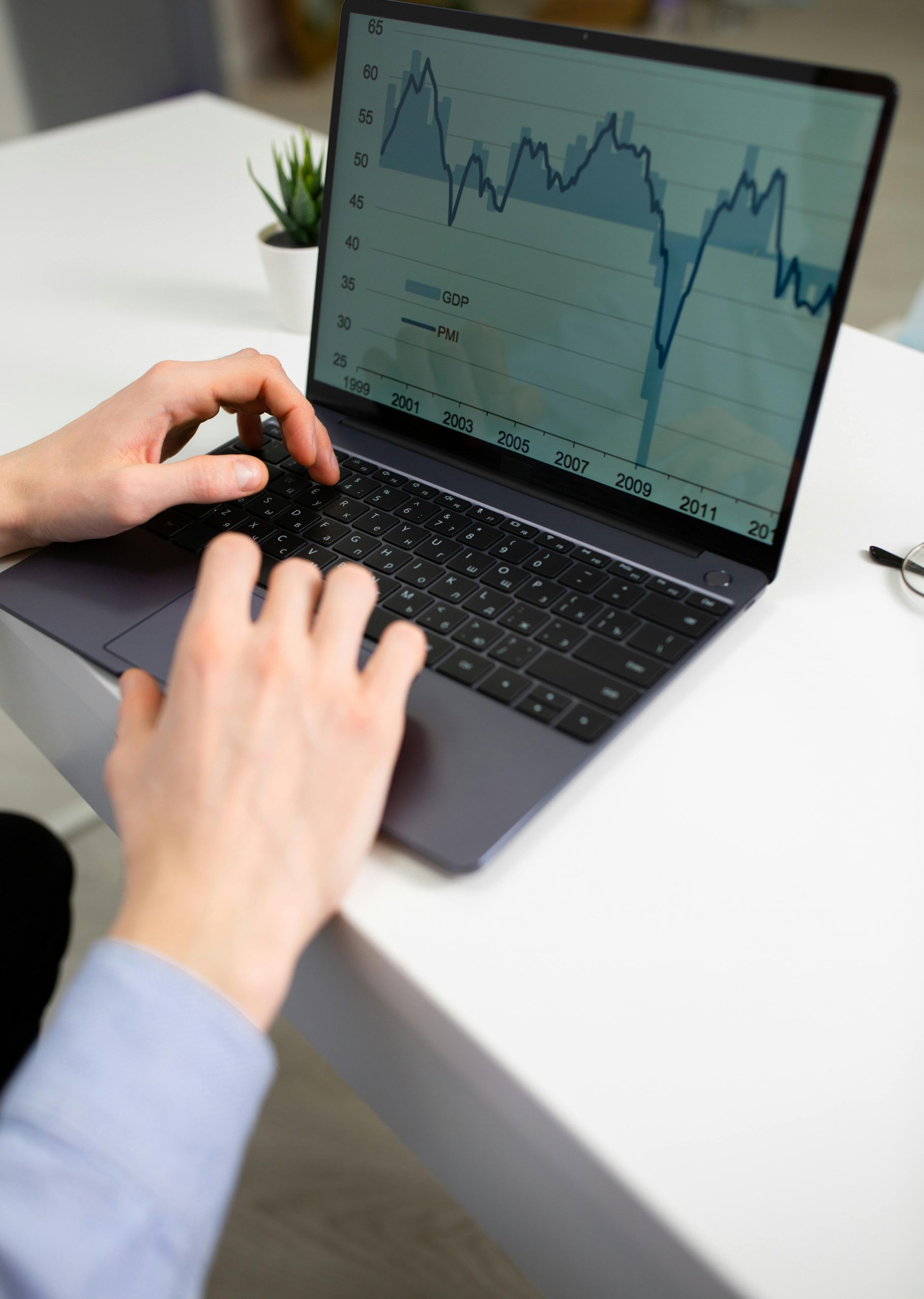 Crop unrecognizable male entrepreneur typing on laptop keyboard while preparing financial diagrams during work in office