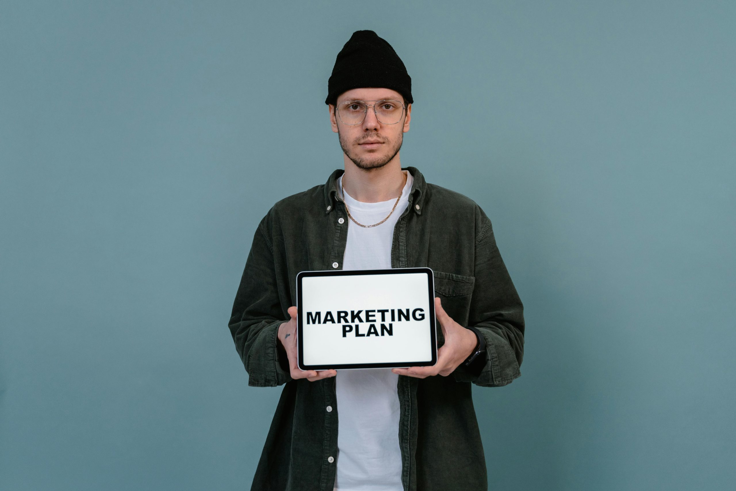 Caucasian man wearing beanie holds a digital marketing plan on a tablet.