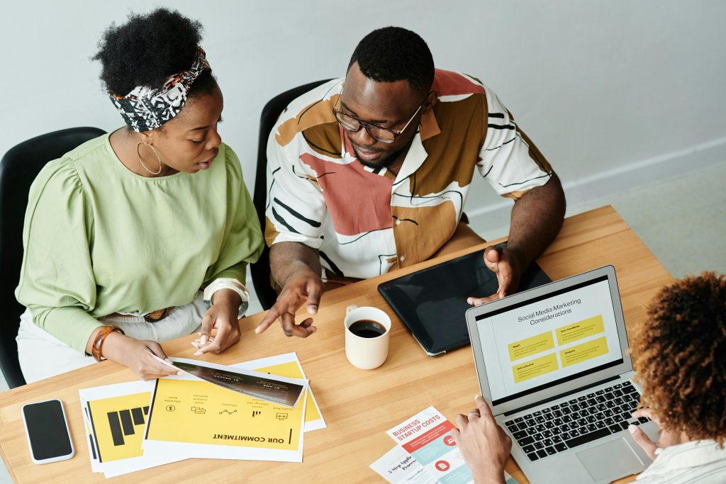 Three colleagues collaborate over marketing documents and a laptop in a modern office setting.