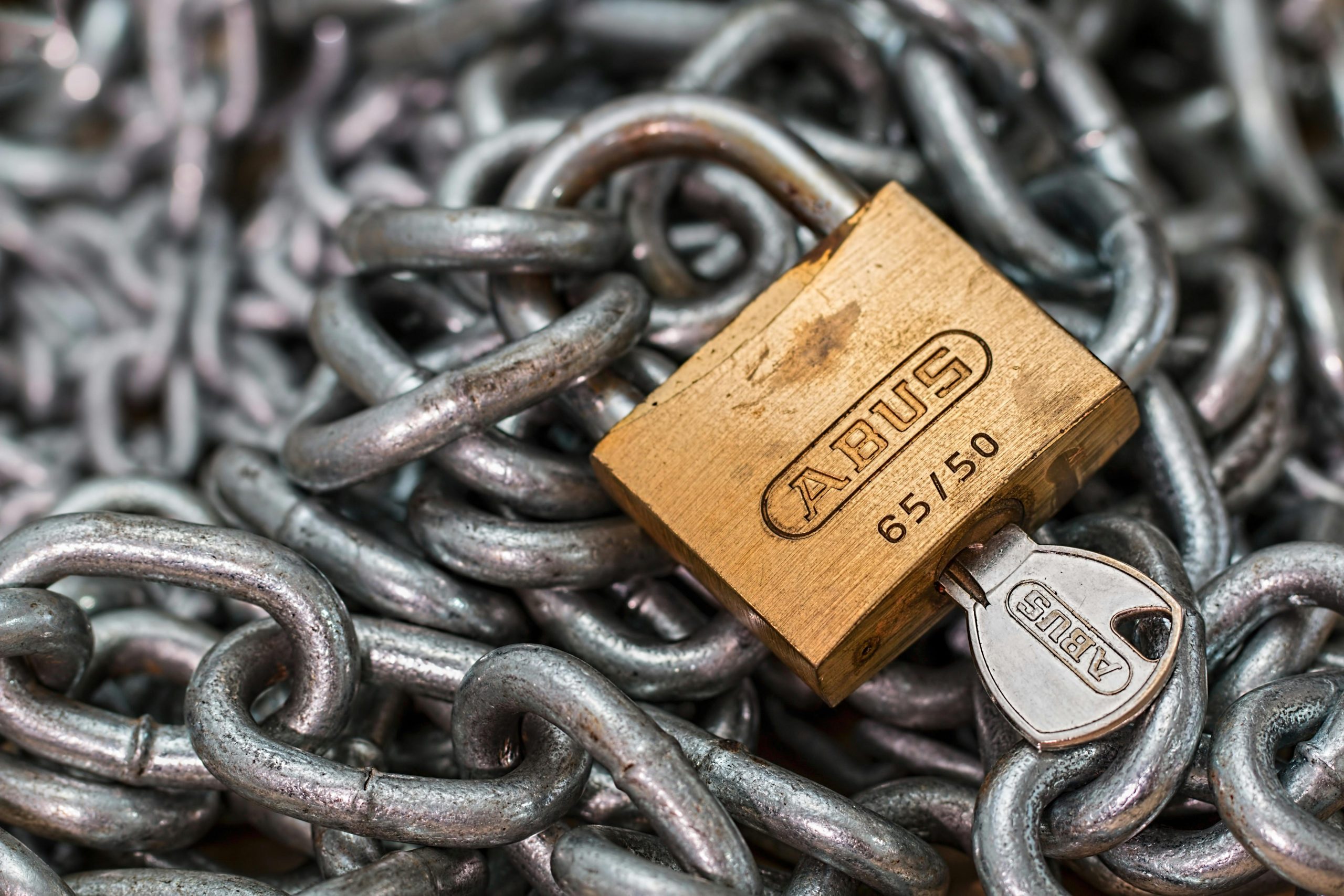 A detailed macro shot of a brass padlock with a key on heavy steel chains, symbolizing security and protection.