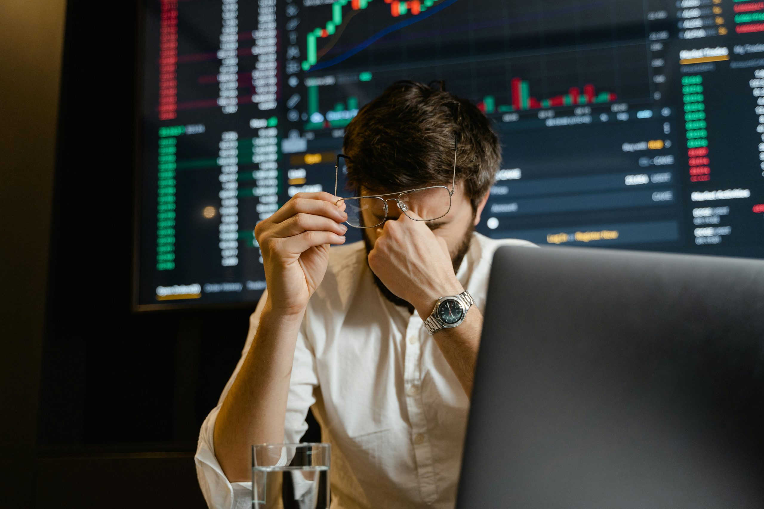 A stressed man looks at stock market data on his computer screen in an office setting.